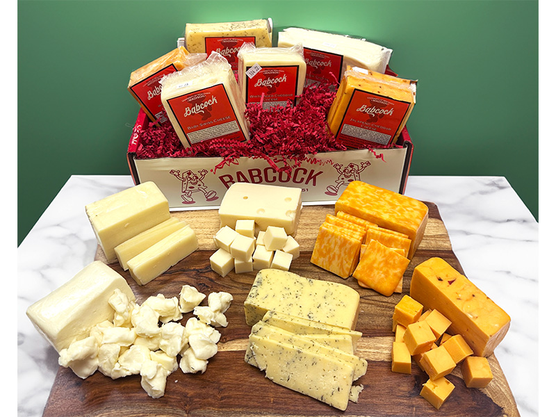 A cheese gift box is shown along with a variety of cut cheese on a cutting board.