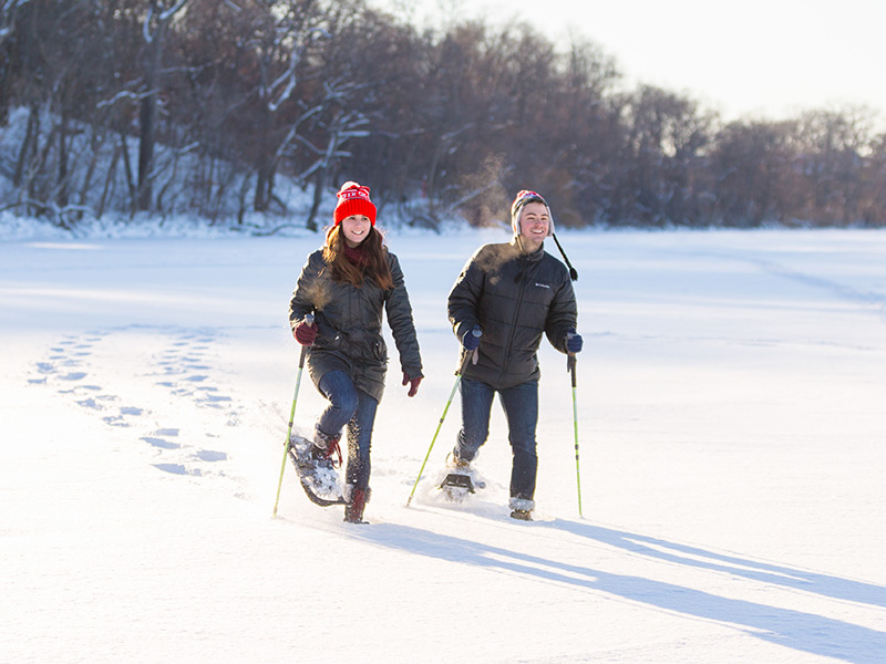 Two people snowshoe on a snowy, frozen lake.