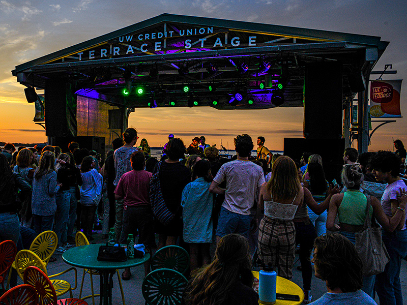 An audience stands around the Terrace Stage, listening to a band at sunset.